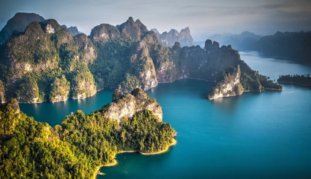 Limestone karsts rising from emerald water of Cheow Lan Lake at sunrise